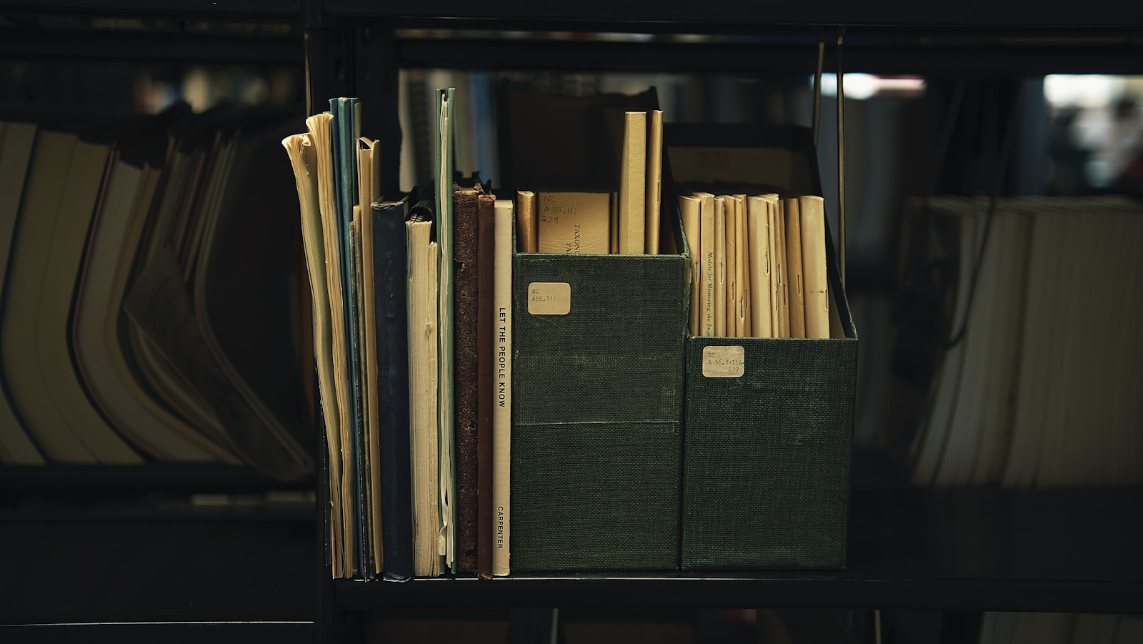 A shelf of old bound files and papers stacked in archive-style boxes with handwritten labels