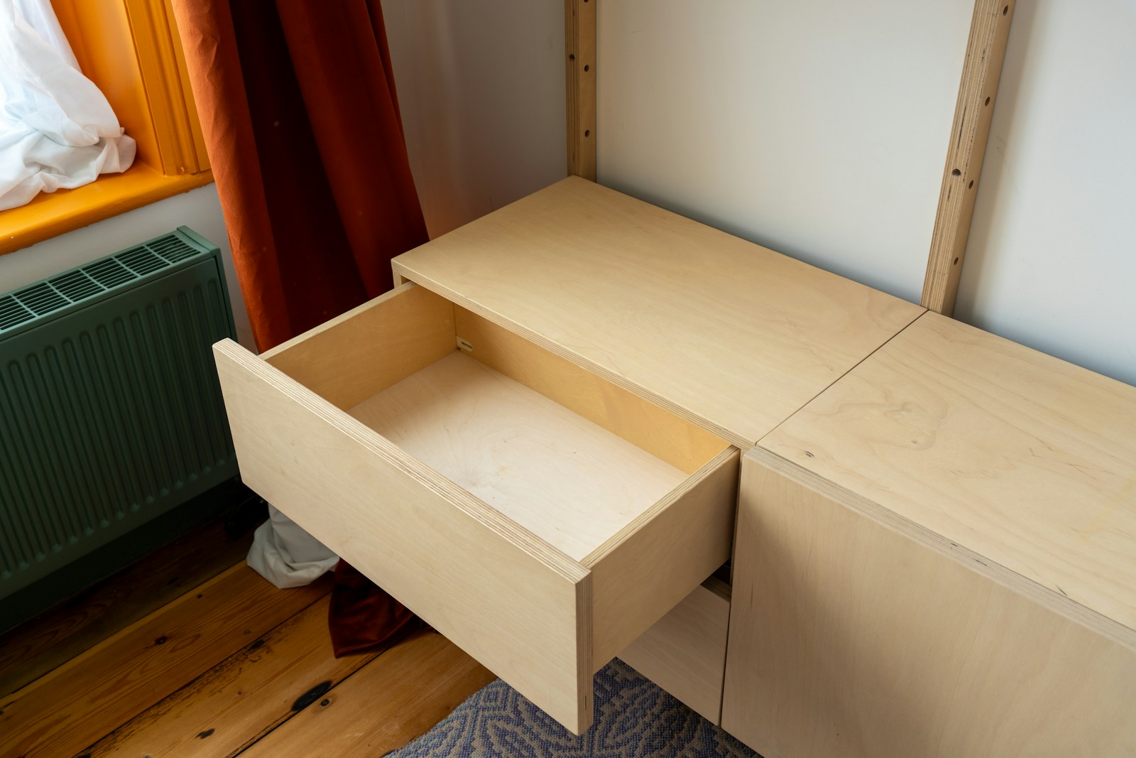 An open wooden drawer built into a light plywood cabinet in a bedroom corner