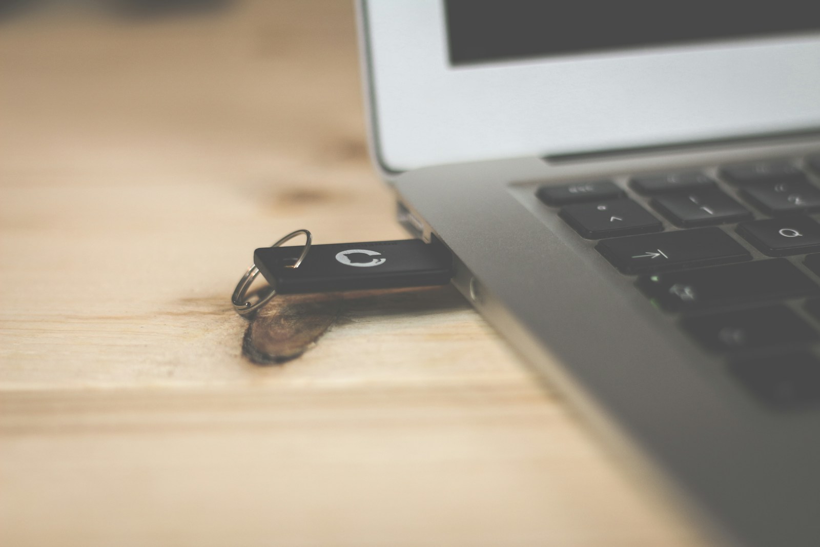 A black USB flash drive on a keyring resting against the edge of an open laptop