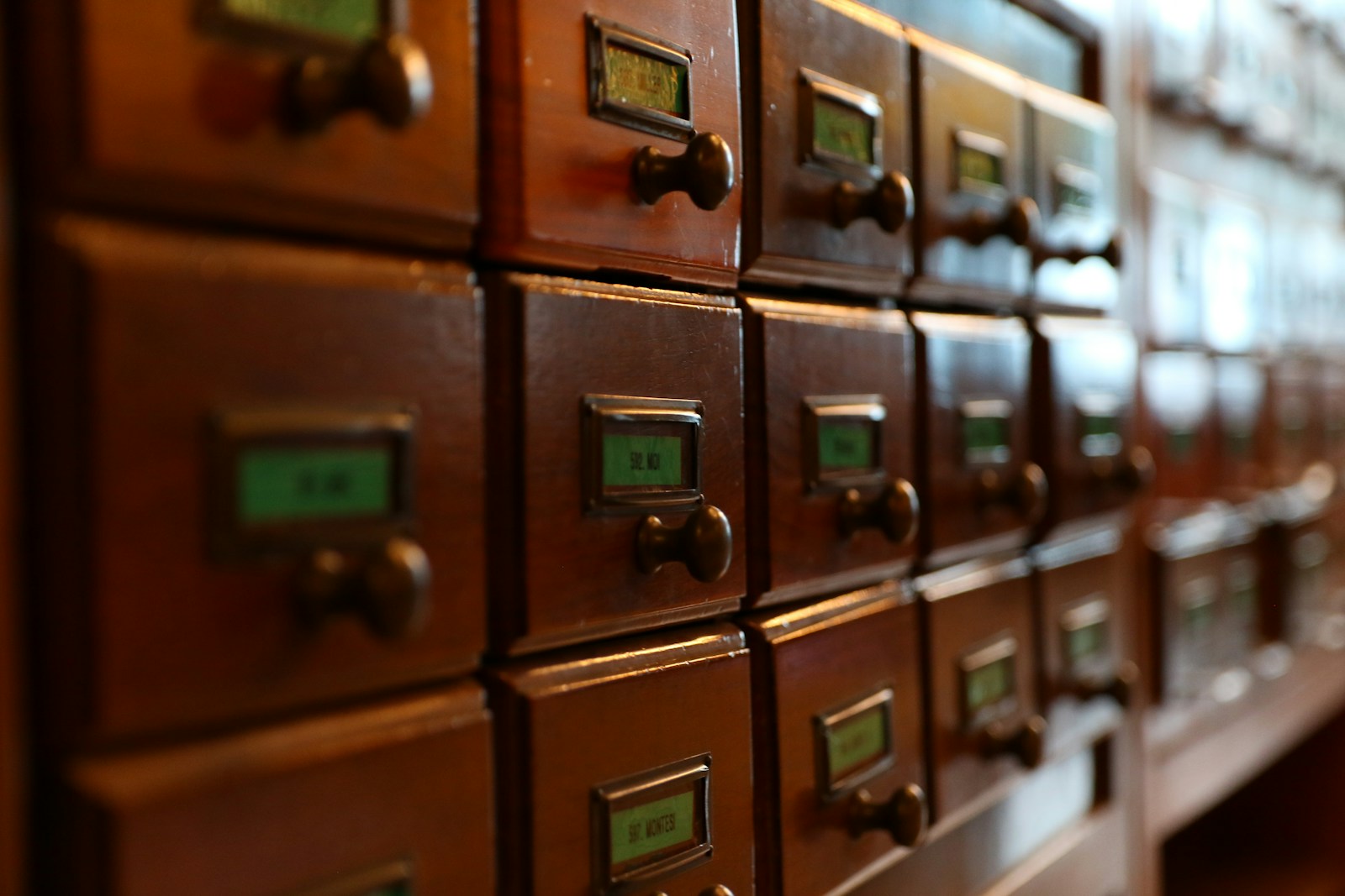 Rows of vintage wooden card catalog drawers with small green paper labels in metal frames