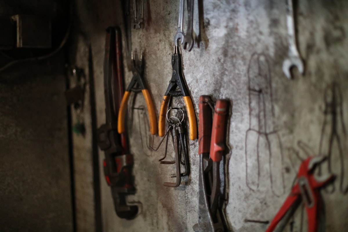 Pliers and wrenches hanging on a workshop wall with their outlines marked behind them