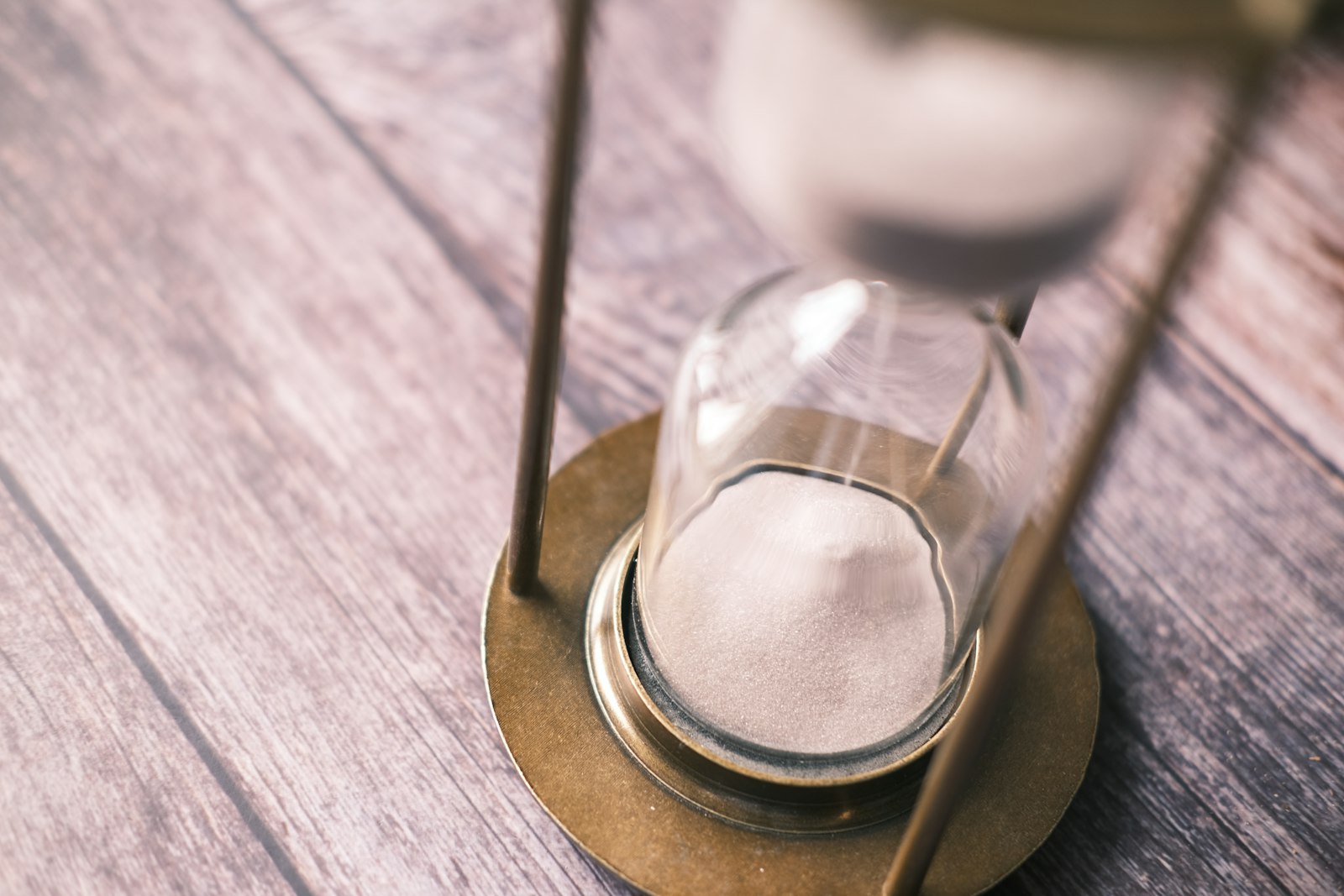 A close-up of an hourglass with sand collecting at the bottom, on a wooden table