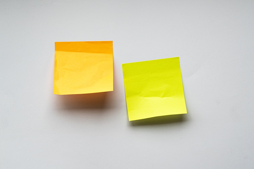 Two sticky notes, one orange and one yellow, placed on a plain wall
