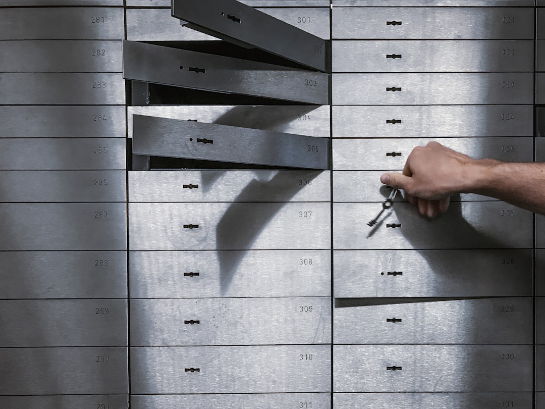 Rows of steel safe deposit boxes in a bank vault, one open with a key in hand