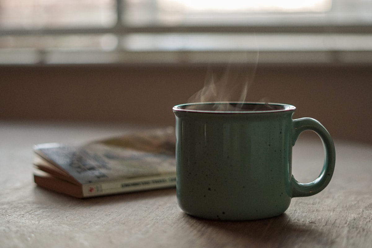 A steaming mug of coffee on a wooden table beside a book on a quiet morning, representing a short weekly planning ritual