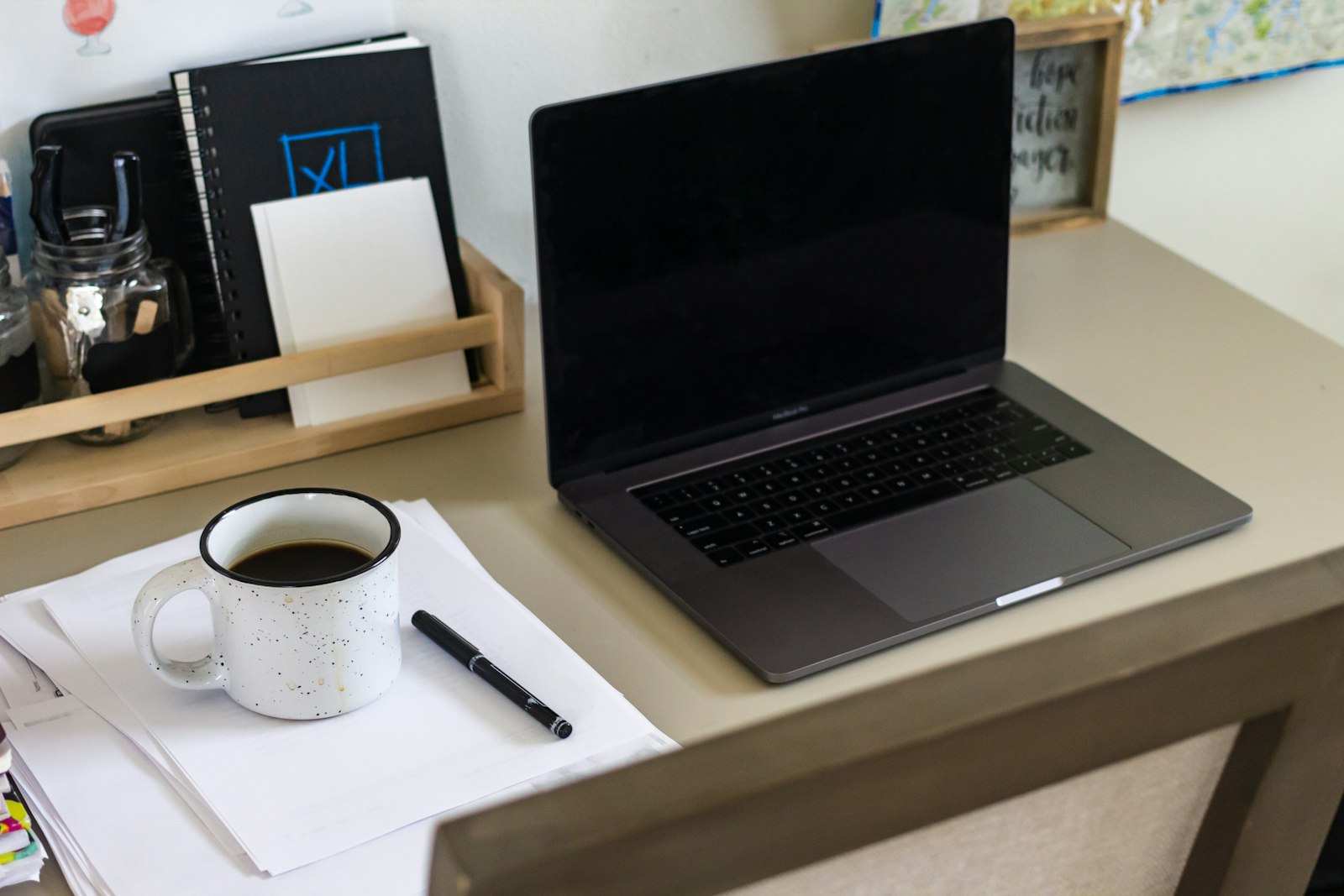 Home office desk with an open laptop, a mug of coffee, a pen, and papers