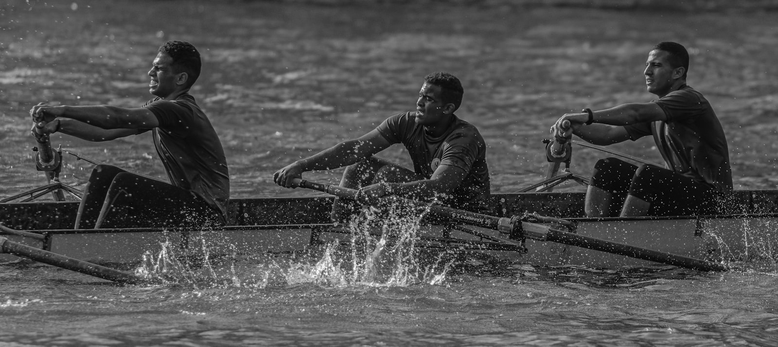 A three-person rowing crew pulling together on a river