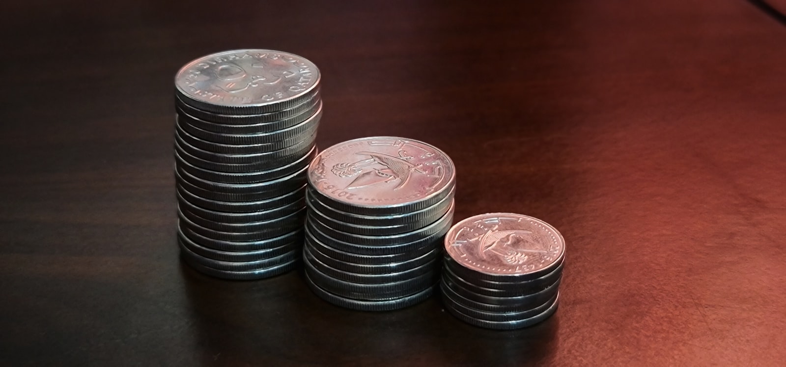 Three stacks of coins on a wooden surface, arranged from small to large