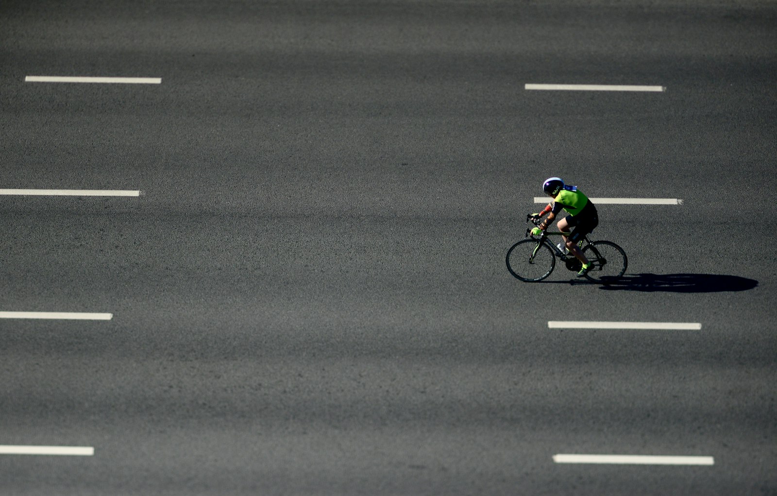 A single cyclist riding alone on a wide, empty road