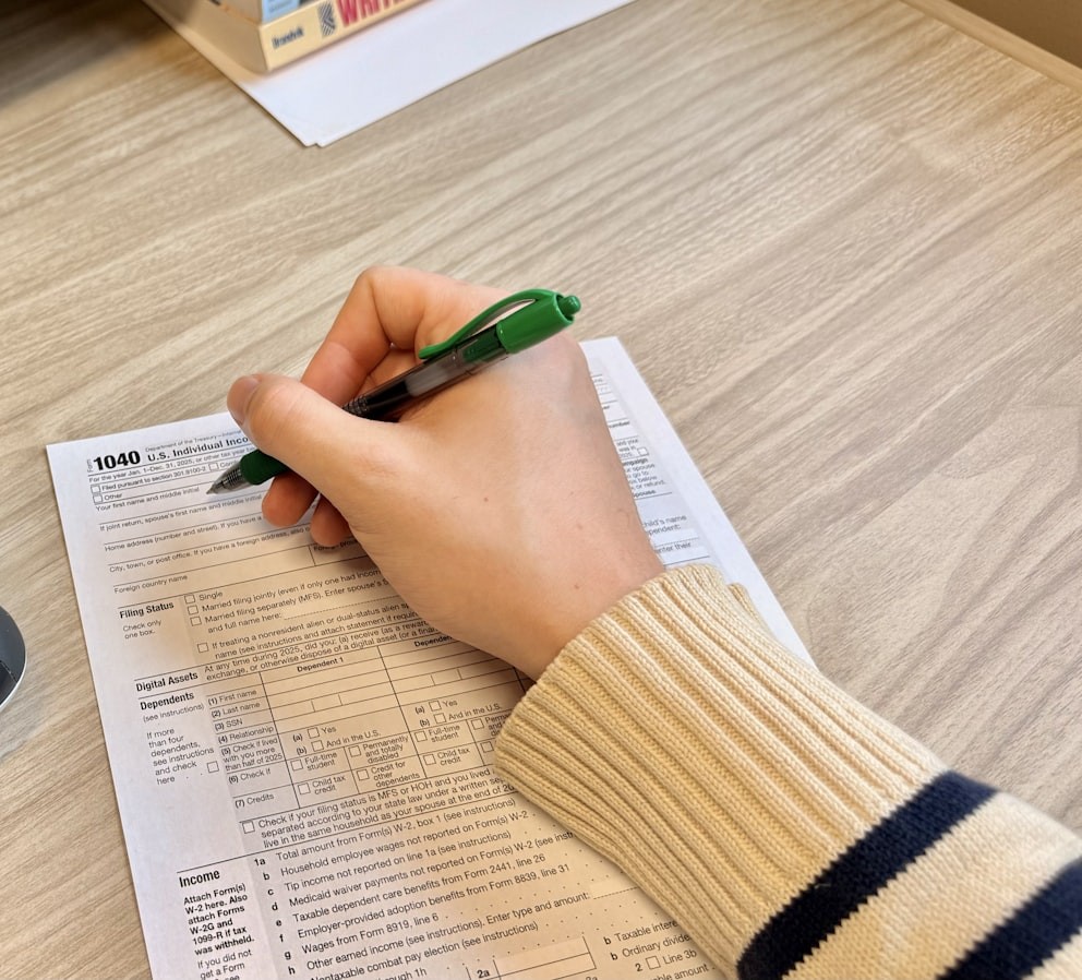 A hand writing on a printed IRS Form 1040 tax return on a desk