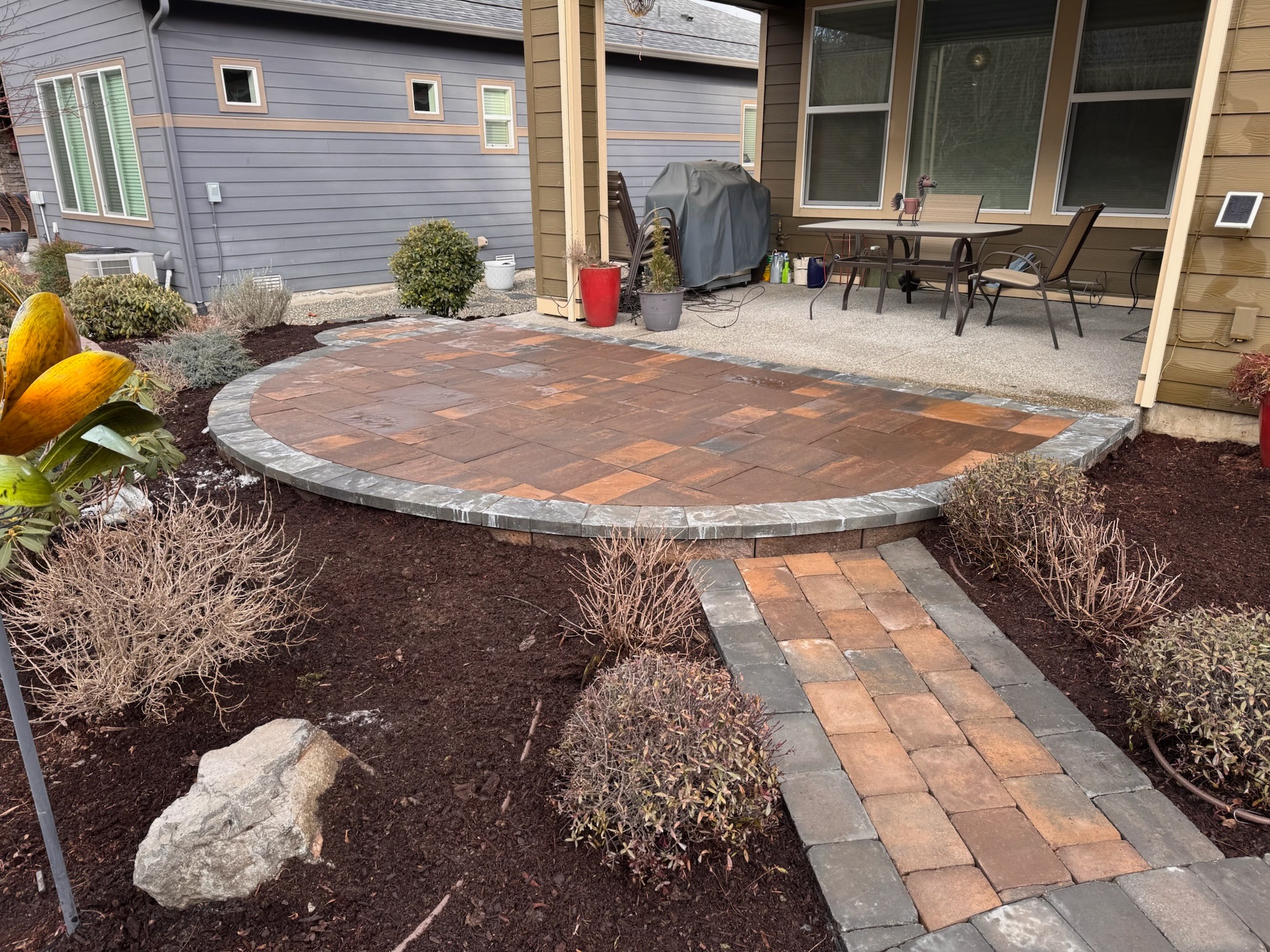 Brick patio and retaining wall by Todd's Nursery in Puyallup, WA, featuring shrubs and a modern outdoor setup.