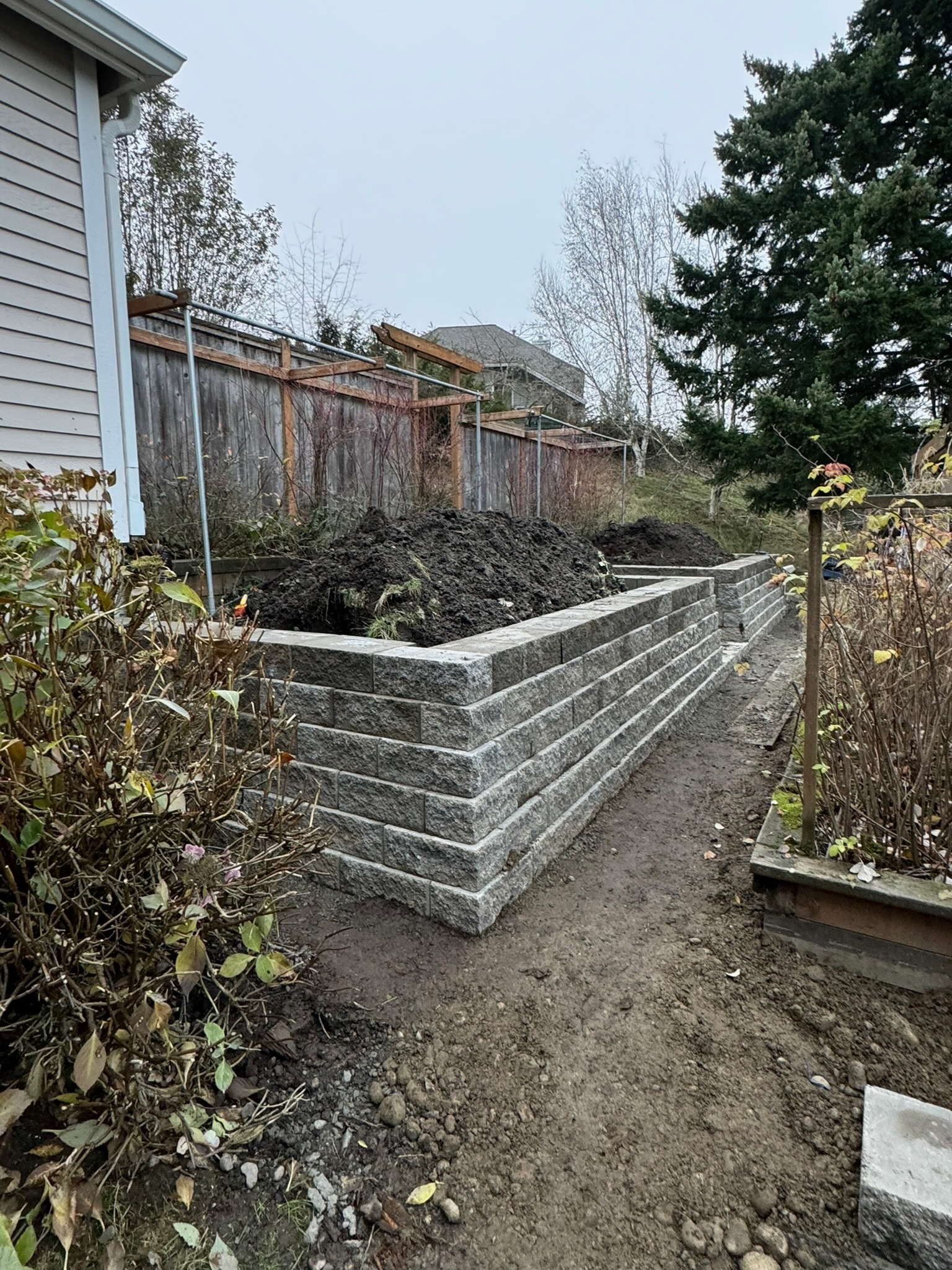 Retaining wall with concrete blocks by Todd's Nursery in Puyallup, WA, surrounded by shrubs and trees.