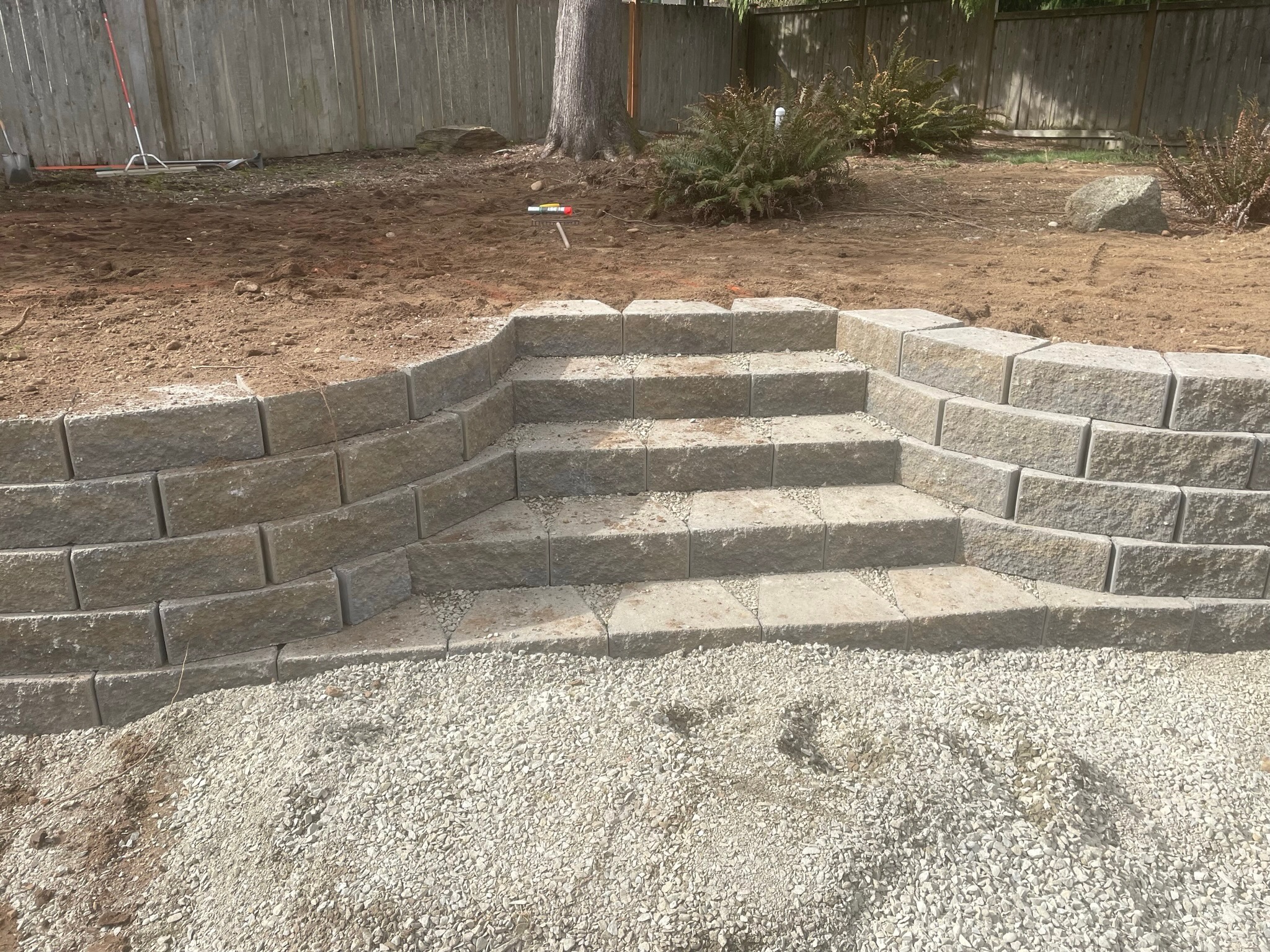 Stone retaining wall with steps by Todd's Nursery in Puyallup, WA, featuring gravel base and surrounding plantings.