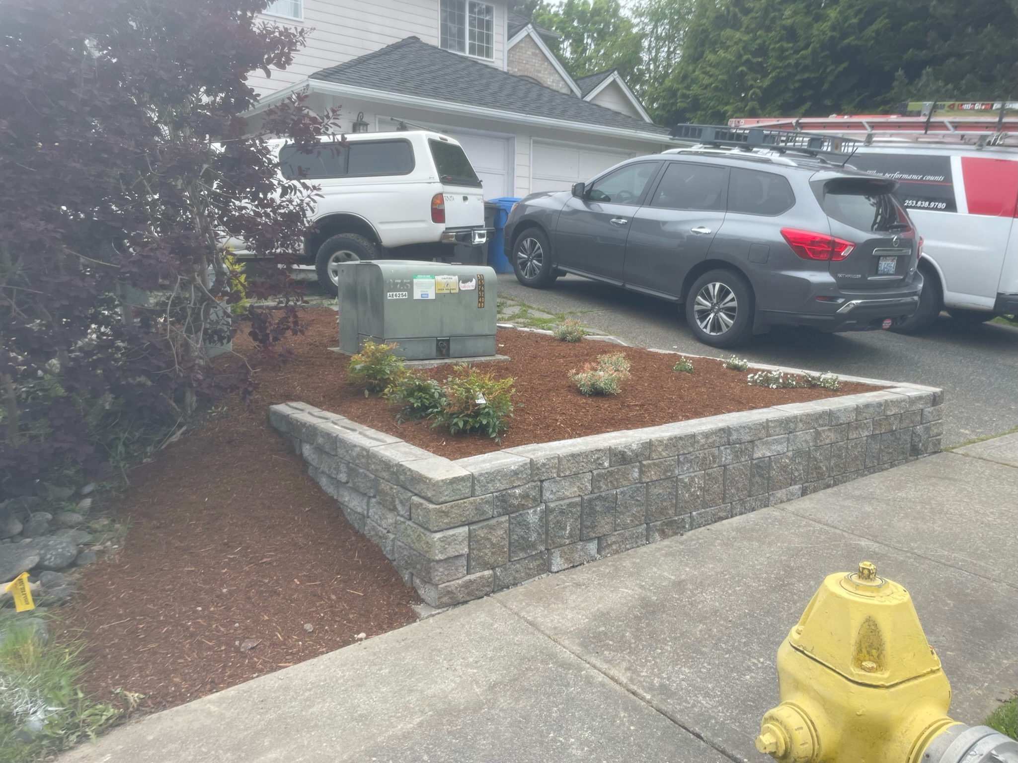 Retaining wall with shrubs by Todd's Nursery in Puyallup, WA, featuring stone blocks and mulch.