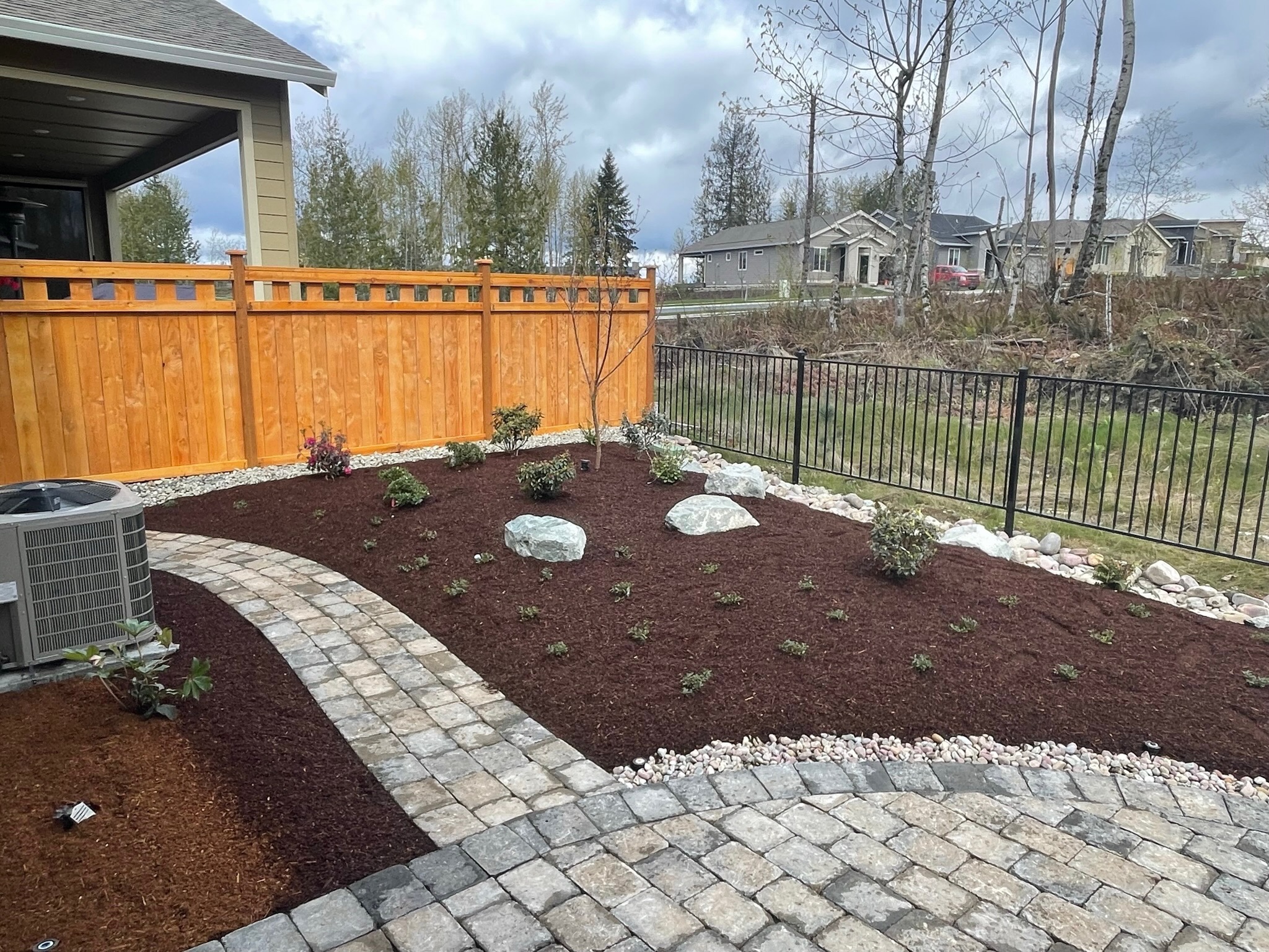 Landscaping by Todd's Nursery in Puyallup featuring a stone path, shrubs, and wooden fence
