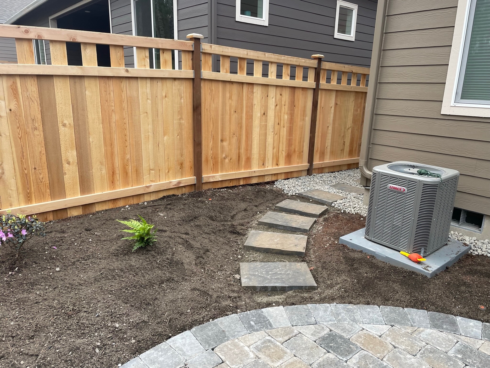 Landscaping by Todd's Nursery in Puyallup featuring a stone path, ferns, and a wooden fence.