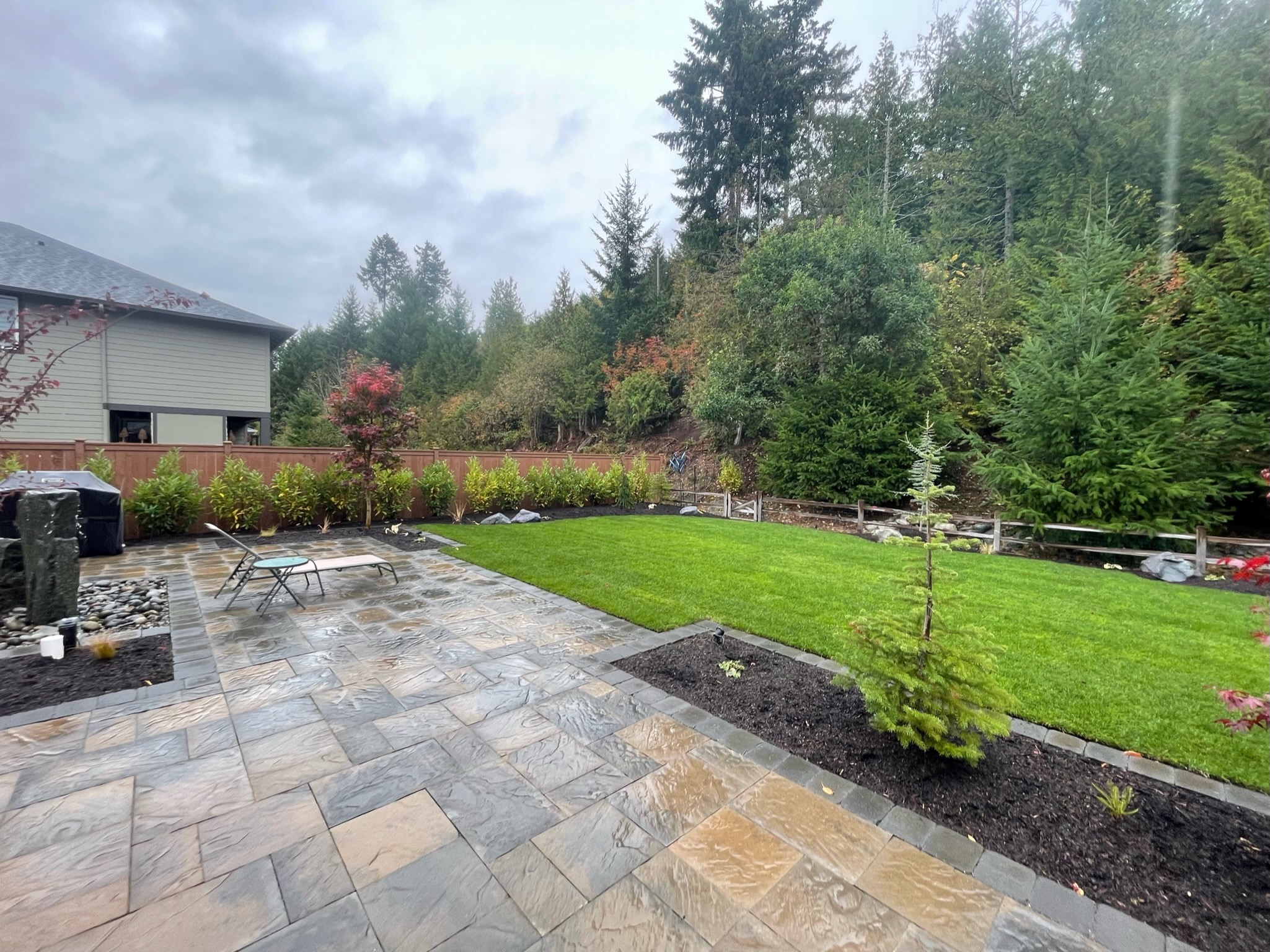 Patio with stone tiles, lush lawn, and trees at Todd's Nursery in Puyallup, WA