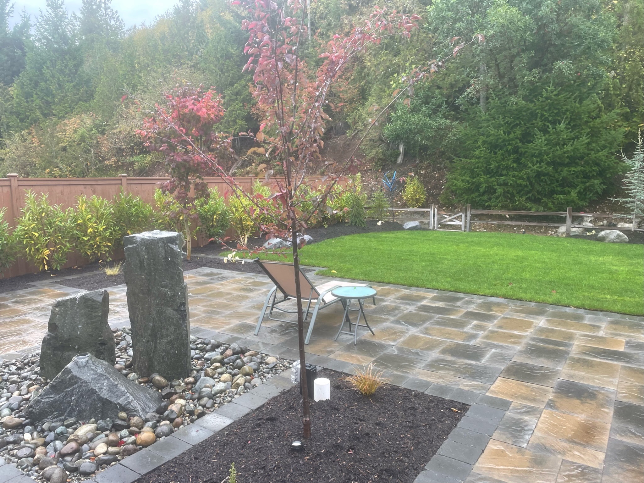 Patio with stone water feature, lush lawn, and trees at Todd's Nursery in Puyallup, WA