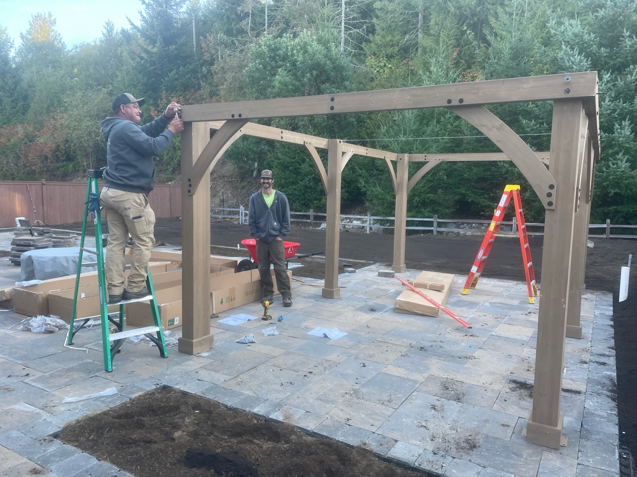 Todd's Nursery pergola installation on stone patio in Puyallup, WA with workers assembling wooden structure.
