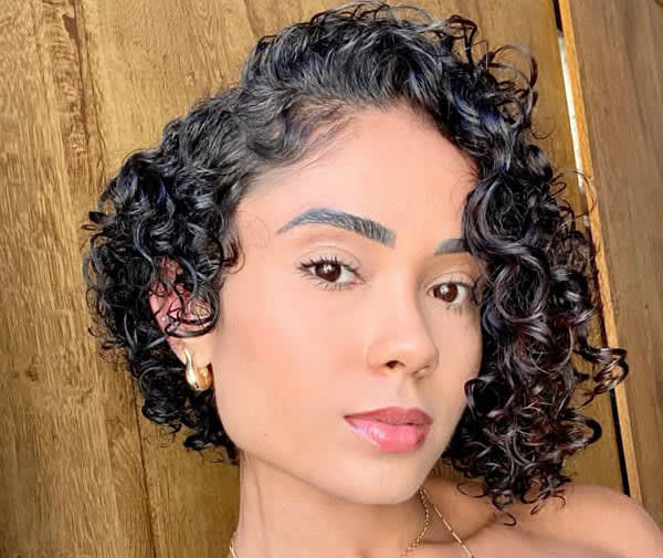 Mulher com cabelo curto cacheado em corte bob assimétrico, destacando a textura natural dos fios.
