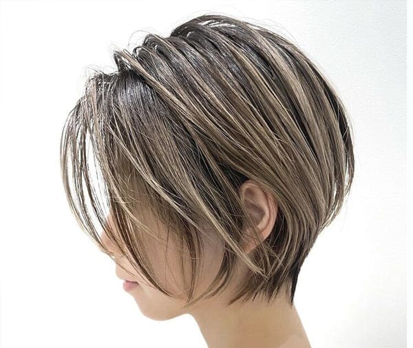Perfil de mulher com cabelo curto liso, mechas iluminadas e franja longa em corte moderno.