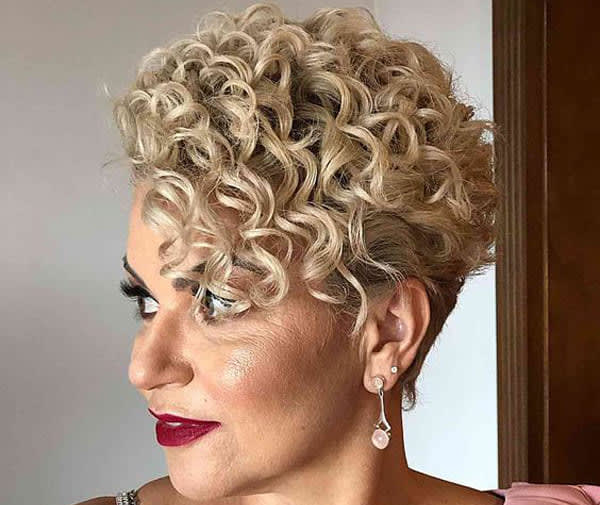 Mulher loira com cabelo curto em corte pixie cacheado, volume no topo e laterais bem curtas.