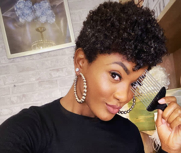Mulher negra sorrindo com cabelo curto em corte pixie crespo, laterais baixas e topo volumoso.