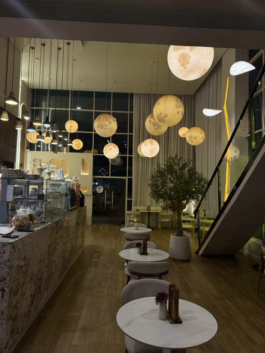 Artisan Blend Kilimani dining room at night with moon-shaped pendant lights, marble tables and an olive tree