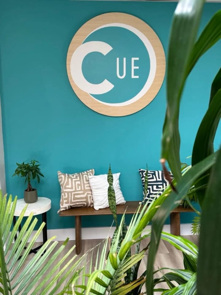 Hand-painted wooden sign for CUE-Up, an education relations firm in Oakland, installed in the office waiting room to welcome visitors with a professional touch.