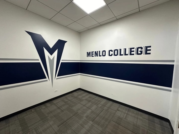 Hand-painted Menlo College wordmark and logo within the athletic office, illustrating custom color application and meticulous design for educational and sports-related signage.
