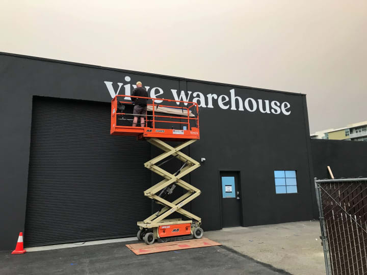 A skilled worker on a scissor lift installs a striking 3D sign at Vive Church Warehouse, showcasing top-tier sign making and installation expertise in action.