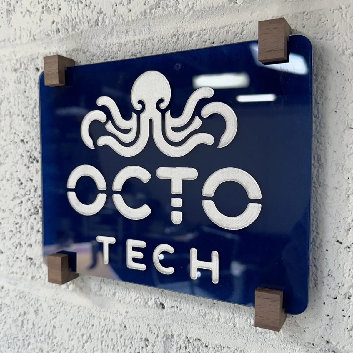 Blue Octotech acrylic office sign held by dark wood mounting blocks.