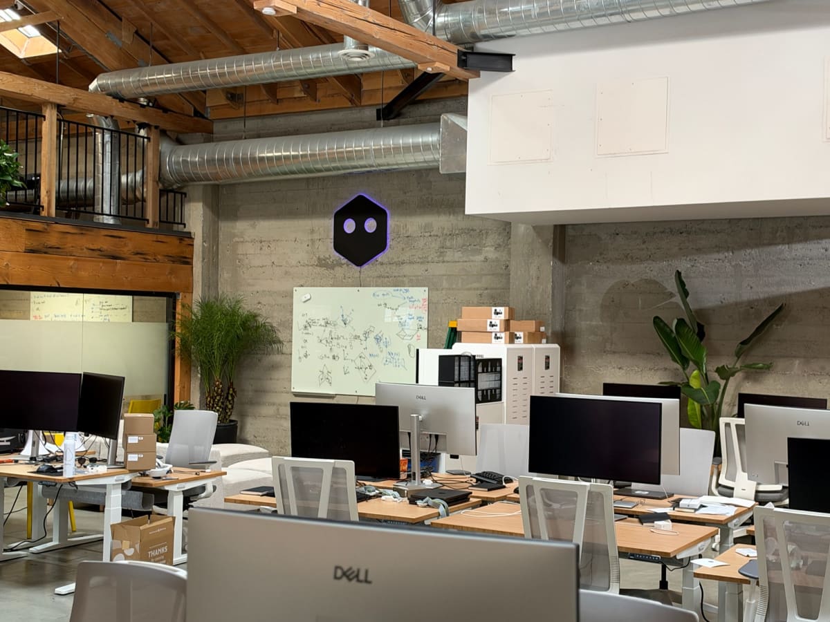 Wide view across office monitors toward the installed purple-lit sign on the far wall