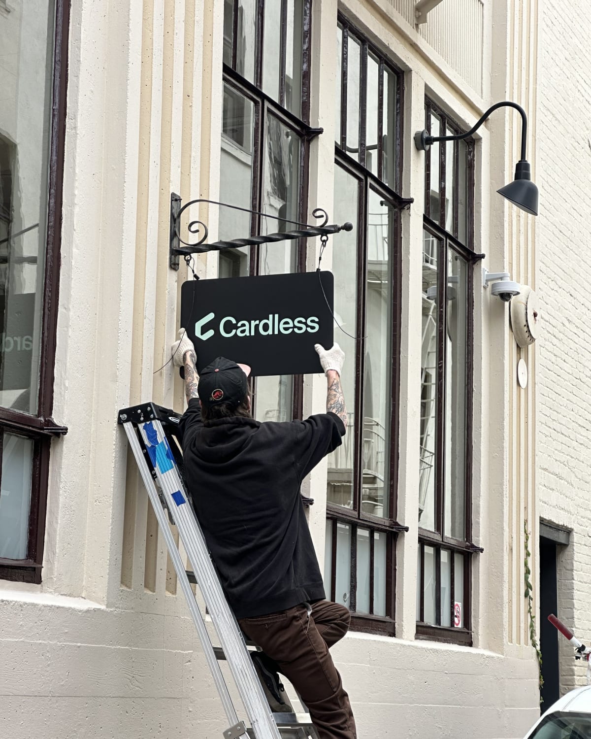 Installer positioning a black anodized aluminum blade sign on a decorative scroll bracket