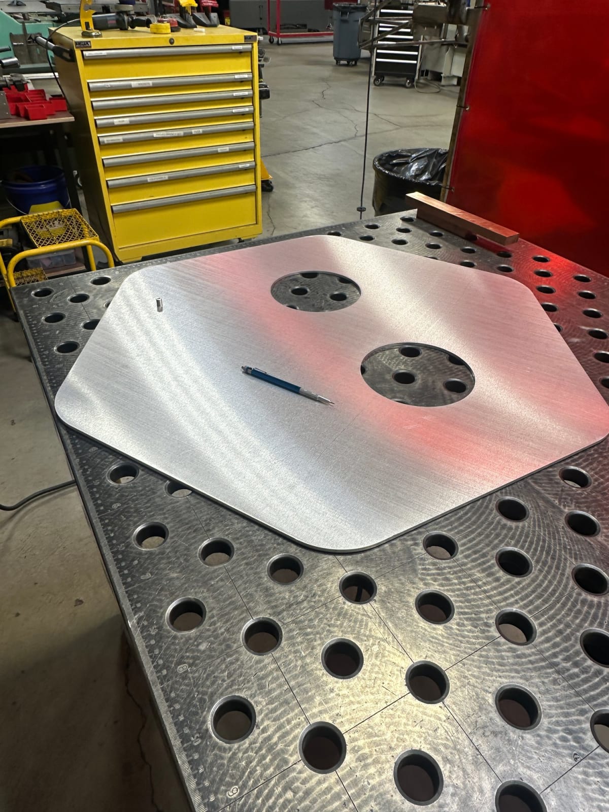 Bare aluminum sign panel with two circular openings and rear mounting points on a welding table