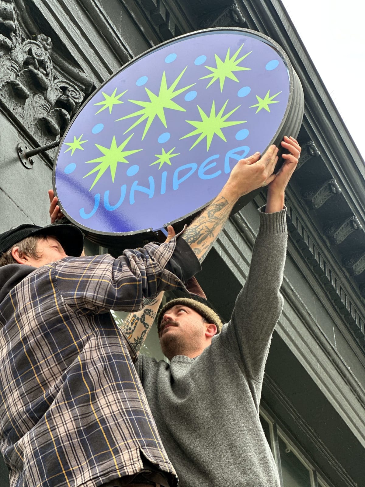 Close-up of installers fastening the round Juniper Cafe blade sign face