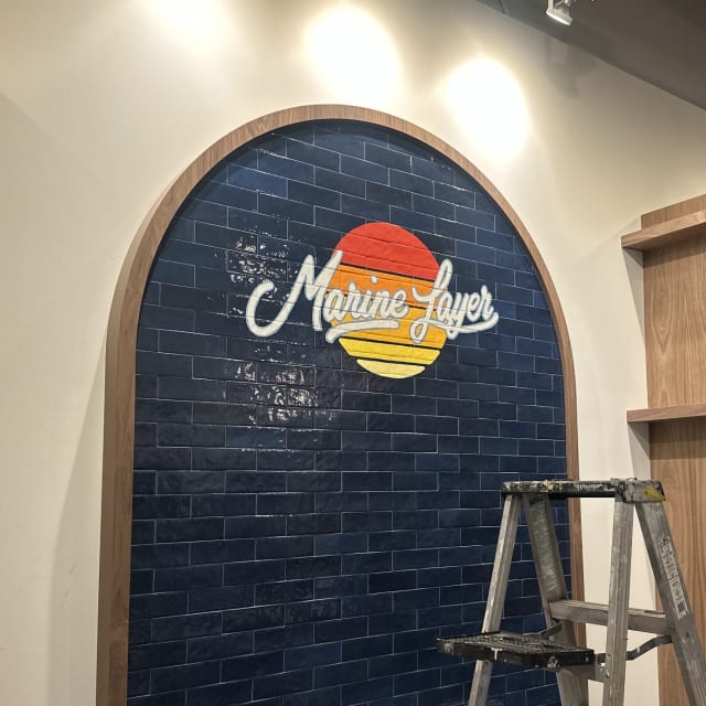 Marine Layer logo inside a dark tiled arch with a ladder nearby in Sacramento