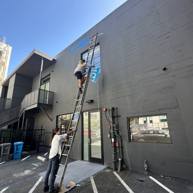 Two crew members using an extension ladder at the Metaview sign installation in Sacramento
