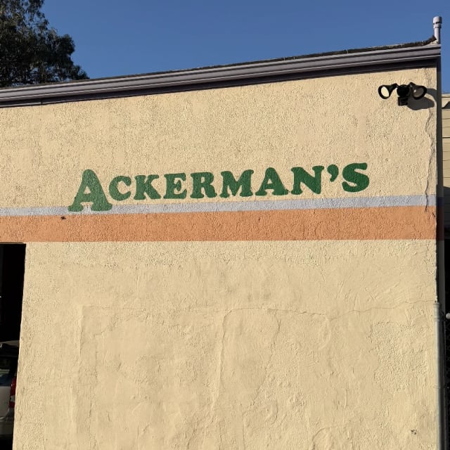 Green Ackerman’s lettering above an orange stripe on a stucco wall