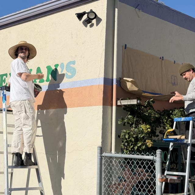 Painter on a stepladder working on Ackerman’s wall lettering in Sacramento