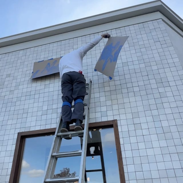 Installer positioning a lettering stencil on an exterior tiled wall