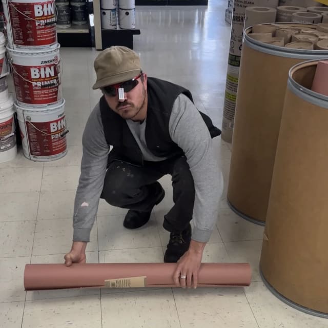 Crew member handling a roll of material in a supply-store aisle