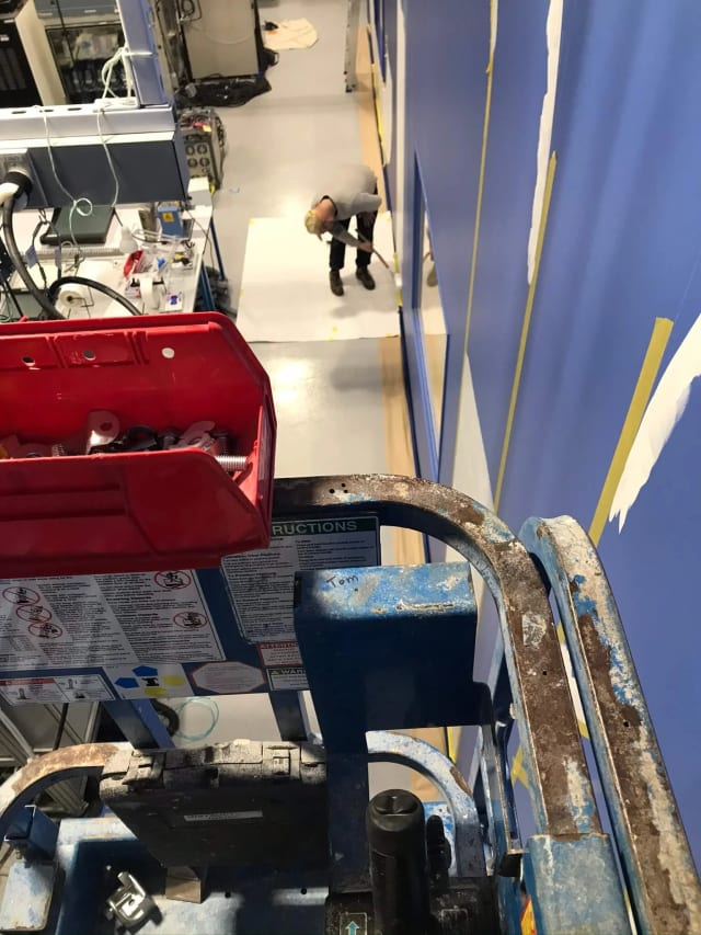 View from a raised lift beside large taped letter outlines on a blue wall