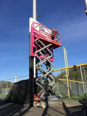 Two workers on a scissor lift painting an elevated field sign