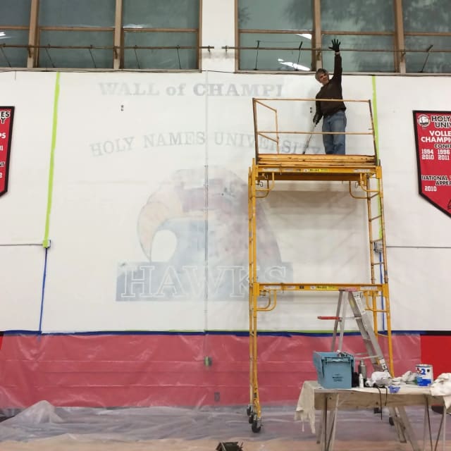 Painter on scaffolding working on wall graphics in a university gym in Sacramento