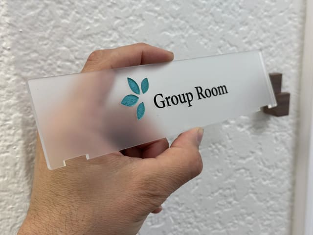 Hands positioning a frosted Group Room plaque in wooden wall brackets for a Sacramento office
