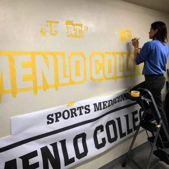 Painter working from a template for Menlo College Sports Medicine lettering