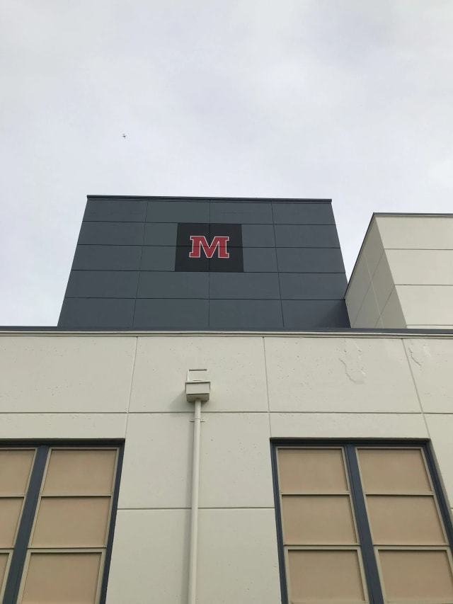 Red M logo near the top of a school building facade