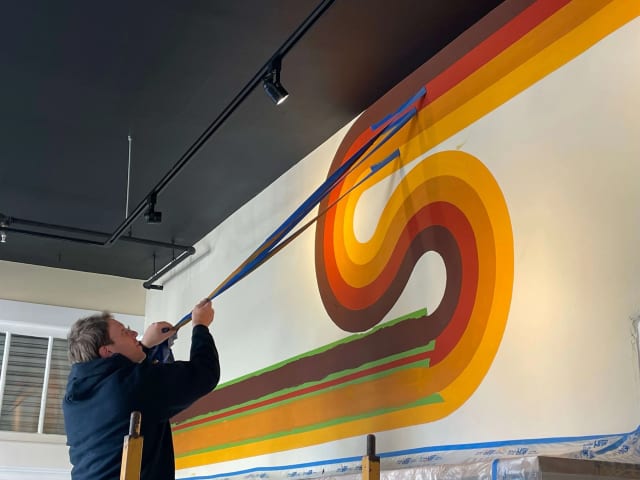 Painter using a long-handled roller on a colorful interior wall graphic