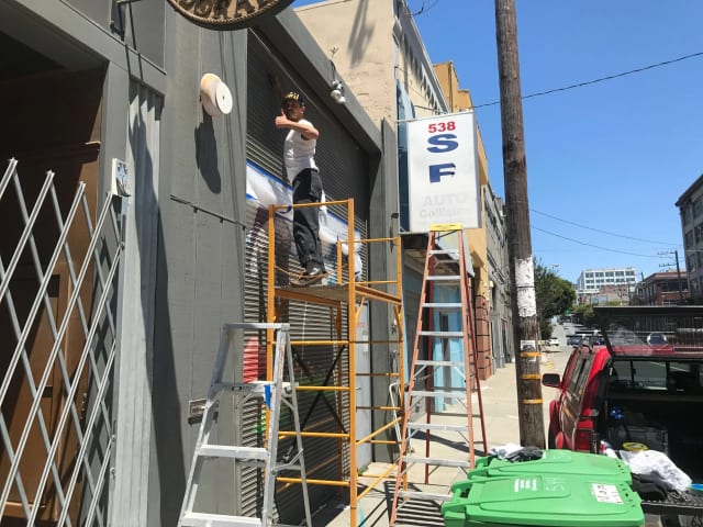 Painter on scaffolding working on lettering beside a commercial entrance on a Sacramento commercial corridor